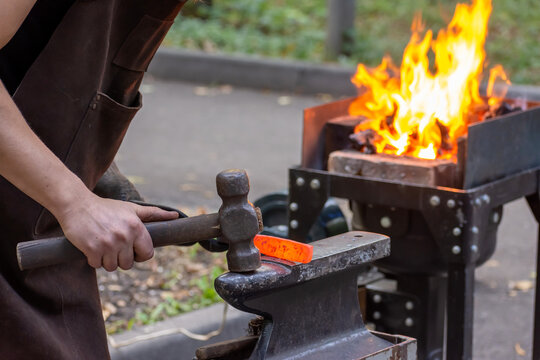 Blacksmith hammering glowing metal next to a blazing forge