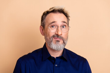 Obraz premium Confident middle-aged businessman with glasses posing against a beige backdrop, wearing a formal blue shirt