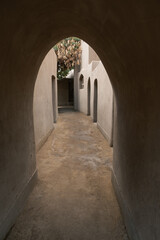 Obraz premium Narrow passageway in an Islamic street with clay buildings. Arched entrance leads to a serene courtyard. Natural light filters through the arch.