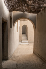 Narrow passageway in an Islamic street with clay buildings. Arched entrance leads to a serene courtyard. Natural light filters through the arch.
