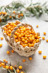 Fresh sea buckthorn berries overflowing a small basket on a textured surface