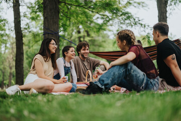 Fototapeta premium A group of young adults enjoying a relaxed and cheerful picnic in a sunny park with trees and greenery surrounding them. They are having fun, laughing, and sharing moments of leisure.