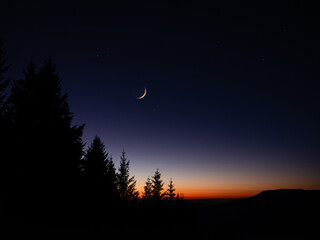 Crescent young Moon with stars, planets and rural countryside tree silhouettes.