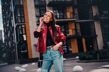 Fashionable young woman in a trendy red jacket and jeans enjoying a sunny day in the city.