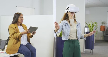 Diverse coworkers testing VR as seated woman guiding user with tablet at office, copy space - Powered by Adobe