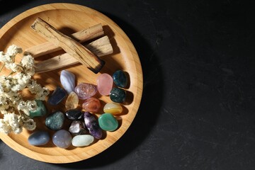 Different beautiful gemstones, palo santo and dried flowers on black table, top view. Space for text