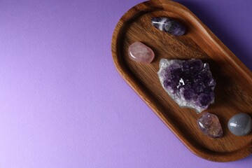 Different beautiful gemstones on purple background, top view. Space for text