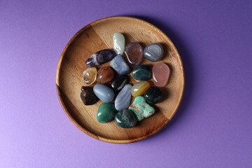 Different beautiful gemstones on purple background, top view