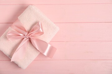 Fresh terry towel with bow on pink wooden background, top view. Space for text