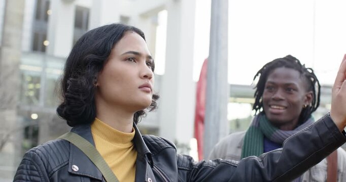 Asian woman holding pole at bus stop noticing African American man approaching, offering coffee cup