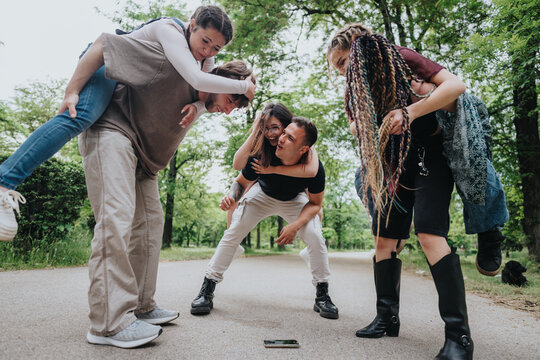 A joyful gathering of friends enjoying themselves together outdoors in a park during daylight. The scene captures bonding moments, laughter, and playful interaction among a group of young adults.
