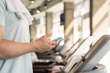 Hands sporty fit man with mobile phone checking apps and fitness progress on running track. Young athlete warm up on treadmill at gym. Close up.