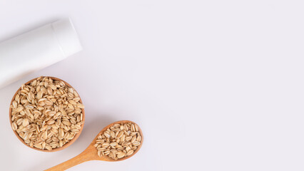 Tube of cream and wooden spoon with oatmeal on light background, skincare concept with copy space, real photo 16:9.