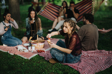 A group of friends spends leisure time having a picnic on a sunny day in a park. They are sitting on a blanket, enjoying food and drinks, surrounded by a vibrant outdoor atmosphere.