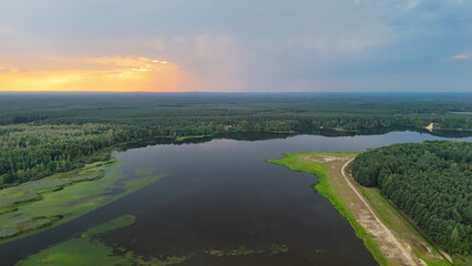 Aerial view of a serene landscape featuring a tranquil lake surrounded by lush greenery and forest....