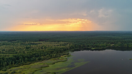 A breathtaking view of a tranquil lake surrounded by lush green forests at sunset. The golden hues of the sky reflect on the water, creating a serene atmosphere.