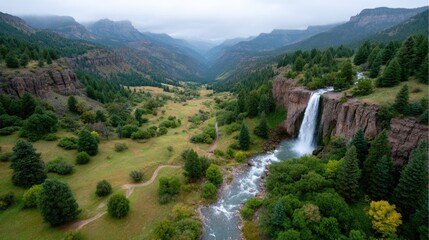 Aerial View of Waterfall Cascading into Canyon with Green Trees and Rocky Cliffs Under Overcast Sky Creates a Cinematic Landscape