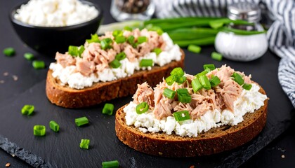 Open-faced sandwiches on dark bread with white cheese and tuna, topped with scallions