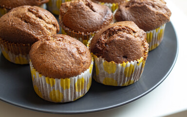 Homemade banana muffins freshly baked in yellow paper cups on dark plate, cozy family baking concept, close up food photography with copy space