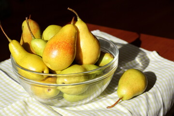 Juicy ripe sweet pears in a glass transparent bowl on a table with a checkered green napkin