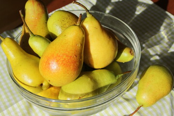 Juicy ripe sweet pears in a glass transparent bowl on a table with a checkered green napkin