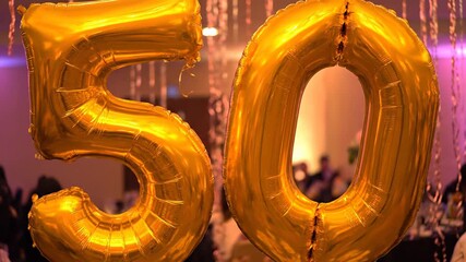 Golden number fifty foil balloons creating a festive atmosphere at a party venue. Bright decorations perfect for a milestone birthday or anniversary bash