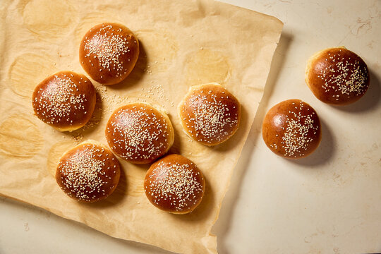 Freshly baked brioche buns with sesame seeds on baking paper. Golden homemade burger buns cooling after baking. - Powered by Adobe