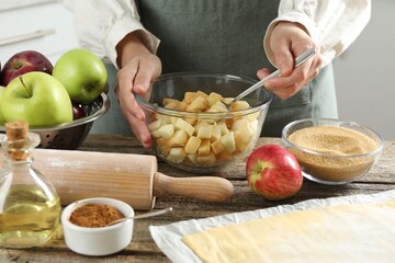 Making delicious apple strudel. Woman mixing ingredients in bowl at wooden table in kitchen, closeup