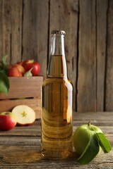 Delicious cider in glass bottle and apples on wooden table
