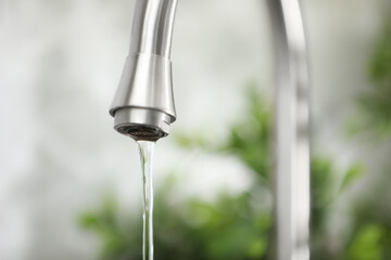 Water saving concept. Stream of water flowing from tap indoors, closeup. Space for text