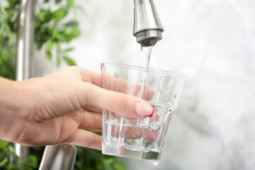 Water saving concept. Woman filling glass with tap water indoors, closeup