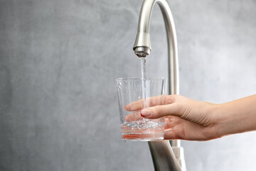 Water saving concept. Woman filling glass with tap water indoors, closeup. Space for text