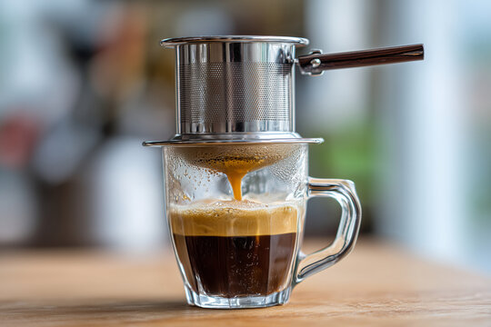 Vietnamese iced coffee dripping through metal phin filter into glass, condensed milk at bottom, 