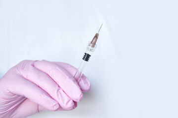 close up of hand in pink medical glove holding syringe with needle against white background.