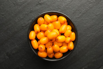 Fresh sea buckthorn berries in bowl on black table, top view