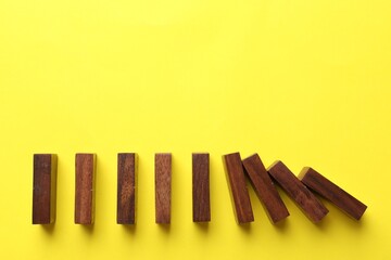 Risk. Wooden blocks falling on yellow background, flat lay with space for text