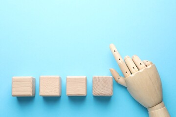 Blank cubes and mannequin hand on light blue background, flat lay. Space for text