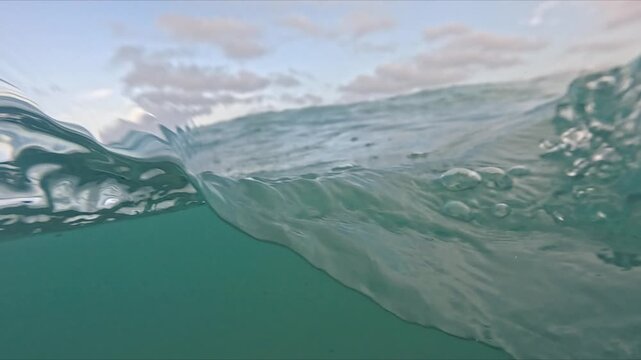 Camera captures half above and half below sea level with visible foam, bubbles and moving waves in slow motion.