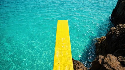 Yellow diving board over clear turquoise water and rocky shore ocean