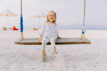 Smiling child girl swinging on swings on sandy beach