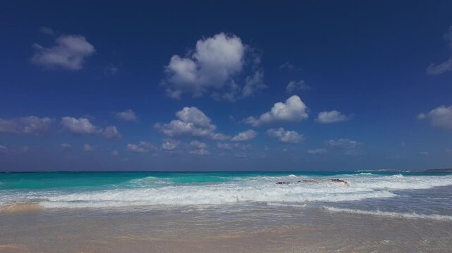 Gentle sea waves roll onto sandy beach beneath deep blue sky with scattered white clouds. Tranquil tropical atmosphere of North Coast of Egypt. Mediterranean sea coastline at Marsa Matrouh governorate