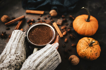 Female hands holding mug of hot chocolate, pumpkins and spices on rustic background, cozy autumn scene