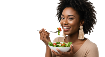 Young african american woman with curls, nude knit top, eating green salad from white bowl in bright white studio, copy space concept of healthy eating and wellness