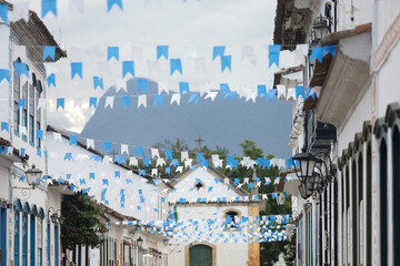 Rua de cidade hist&oacute;rica brasileira decorada com bandeirinhas azuis, destacando arquitetura colonial e atmosfera festiva.