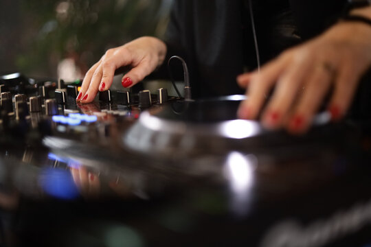 M&atilde;os femininas operando equipamento de DJ durante apresenta&ccedil;&atilde;o musical, destacando tecnologia, ritmo e performance ao vivo.