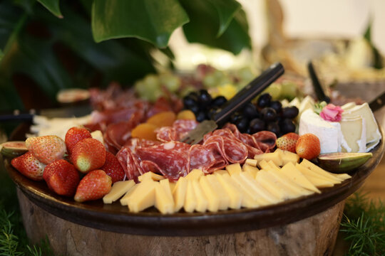 T&aacute;bua de frios com queijos, embutidos e frutas frescas servida em base r&uacute;stica, em ambiente de evento elegante.