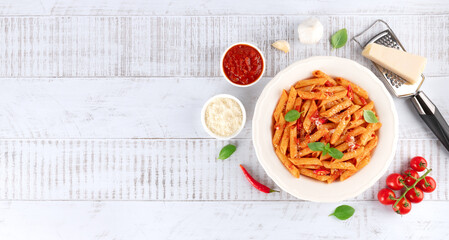 Pasta arrabbiata with tomato sauce, chili, parmesan and basil on wooden background. IItalian cuisine