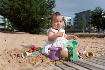young child playing joyfully in a bright sandy playground with toys, amidst urban park environment under clear skies, emphasizing innocence, playfulness, and outdoor fun, environment, freedom, relax