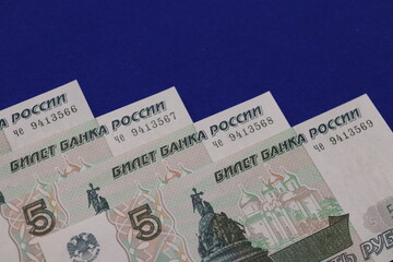 A close-up view of several 5-ruble banknotes from Russia, featuring intricate designs and security features, displayed against a blue background