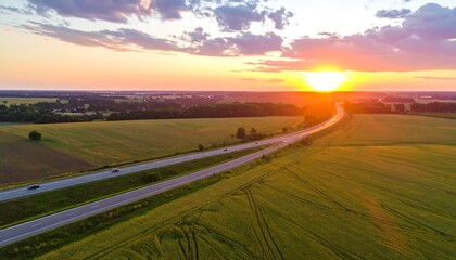 Aerial view of highway cutting through rural land as the sunset paints the sky